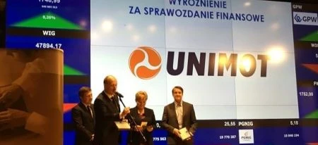 Pracownik umysłowy w garniturze patrzący na urządzenie wyświetlające informacje finansowe. Widoczny jest logo GPW i WIG20. Wyświetlane są dane dotyczące zarządzania i pracy.