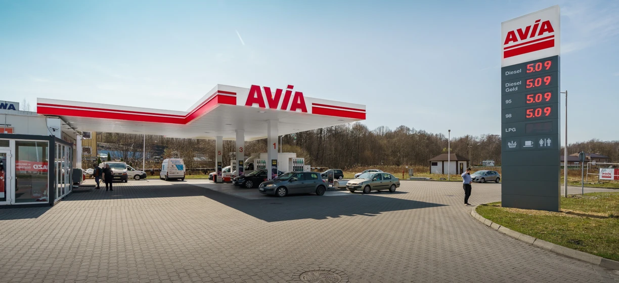 Opis alternatywny obrazu: Samochód rodzinny zaparkowany na stacji benzynowej z terenowym pojazdem sportowym w tle. Widoczne ceny paliwa dla oleju napędowego, benzyny Gold 95, benzyny Gold 98 i LPG.