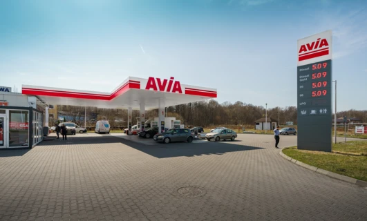 Opis alternatywny obrazu: Samochód rodzinny zaparkowany na stacji benzynowej z terenowym pojazdem sportowym w tle. Widoczne ceny paliwa dla oleju napędowego, benzyny Gold 95, benzyny Gold 98 i LPG.