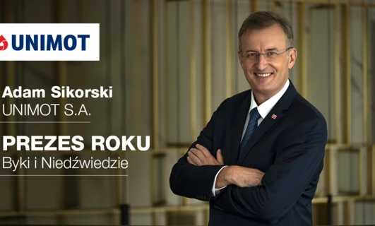Osoba ubrana w biznesową galanterię, nosząca marynarkę, koszulę i krawat, stoi przed znakiem z polskim tekstem upamiętniającym Adama Sikorskiego z UNIMOT S.A. jako Dyrektora Generalnego roku. Pracownik umysłowy w profesjonalnym stroju.